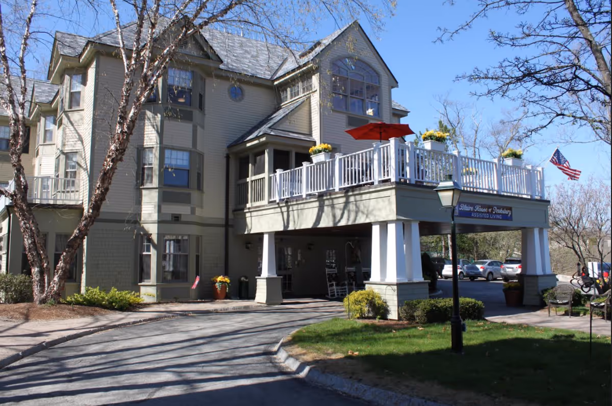 Front exterior of Blaire House of Tewksbury assisted living building with a covered entrance, balcony and an American flag.