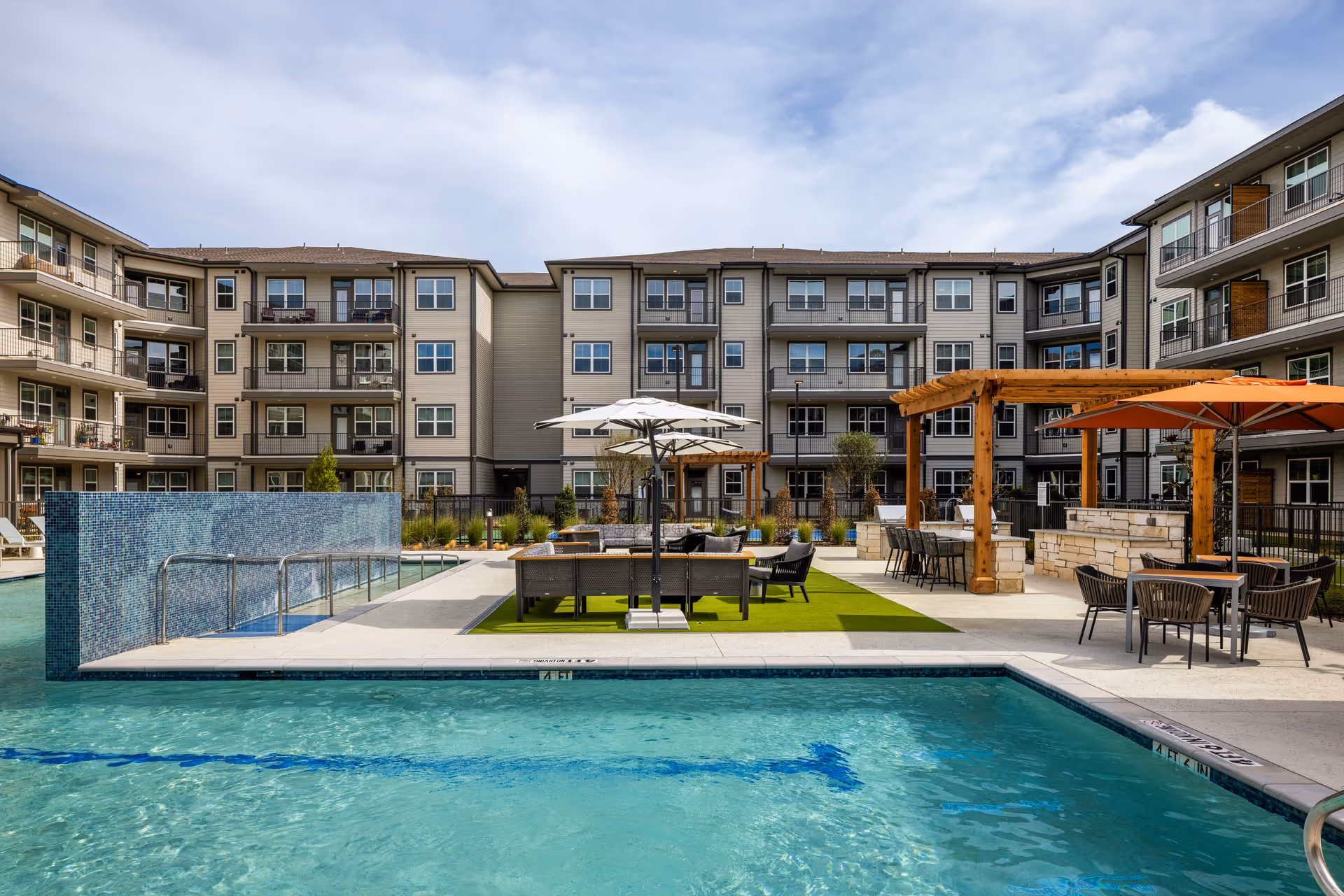 Modern multi-story residential building surrounding an outdoor pool and courtyard with lounge seating, pergolas, and umbrellas.