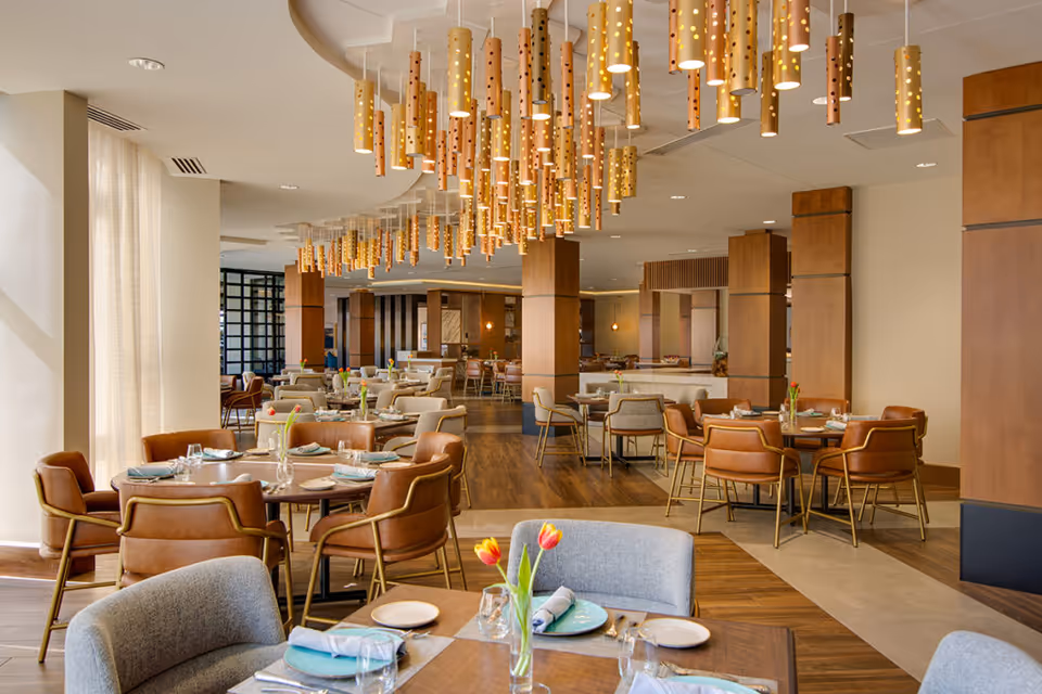 Well-lit dining room with multiple set tables and chairs, decorative hanging pendant lights, and fresh tulip centerpieces.