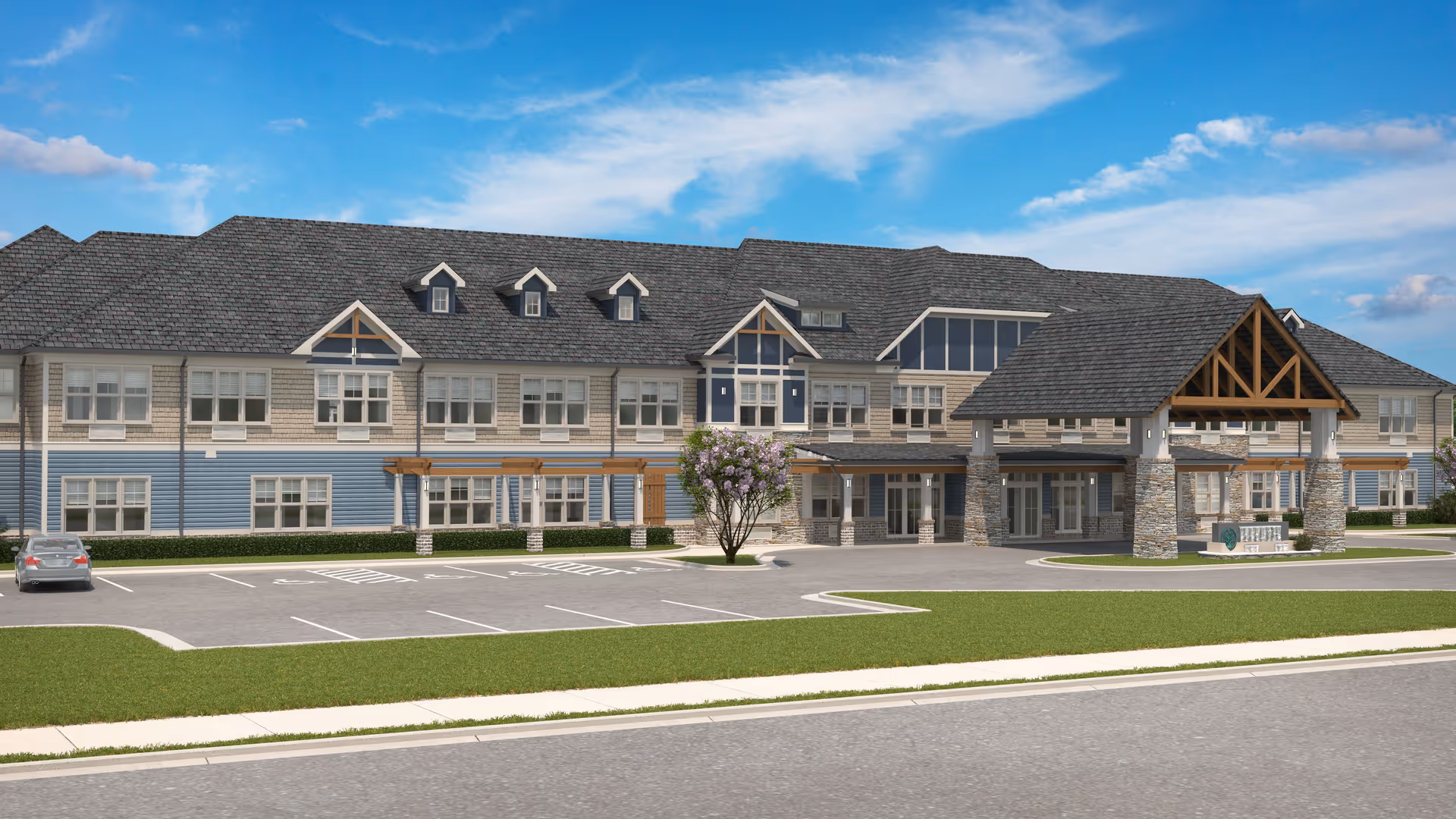 Exterior view of a large two-story senior living facility building with a covered entrance supported by stone pillars, multiple windows, and a parking lot with a single car. The building features a combination of beige and blue siding with a gray shingled roof under a partly cloudy blue sky.
