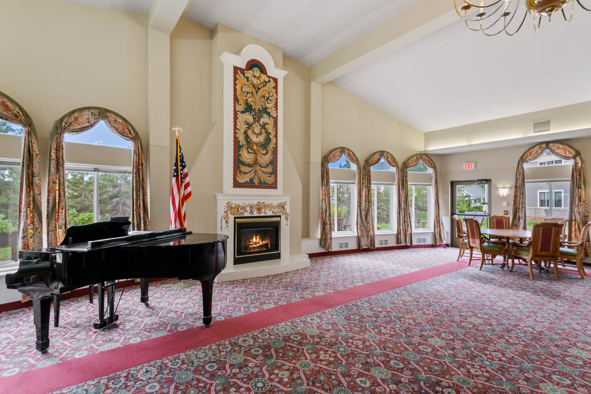 Spacious lounge with a grand piano, fireplace, patterned carpet, arched windows with curtains, and a dining table.