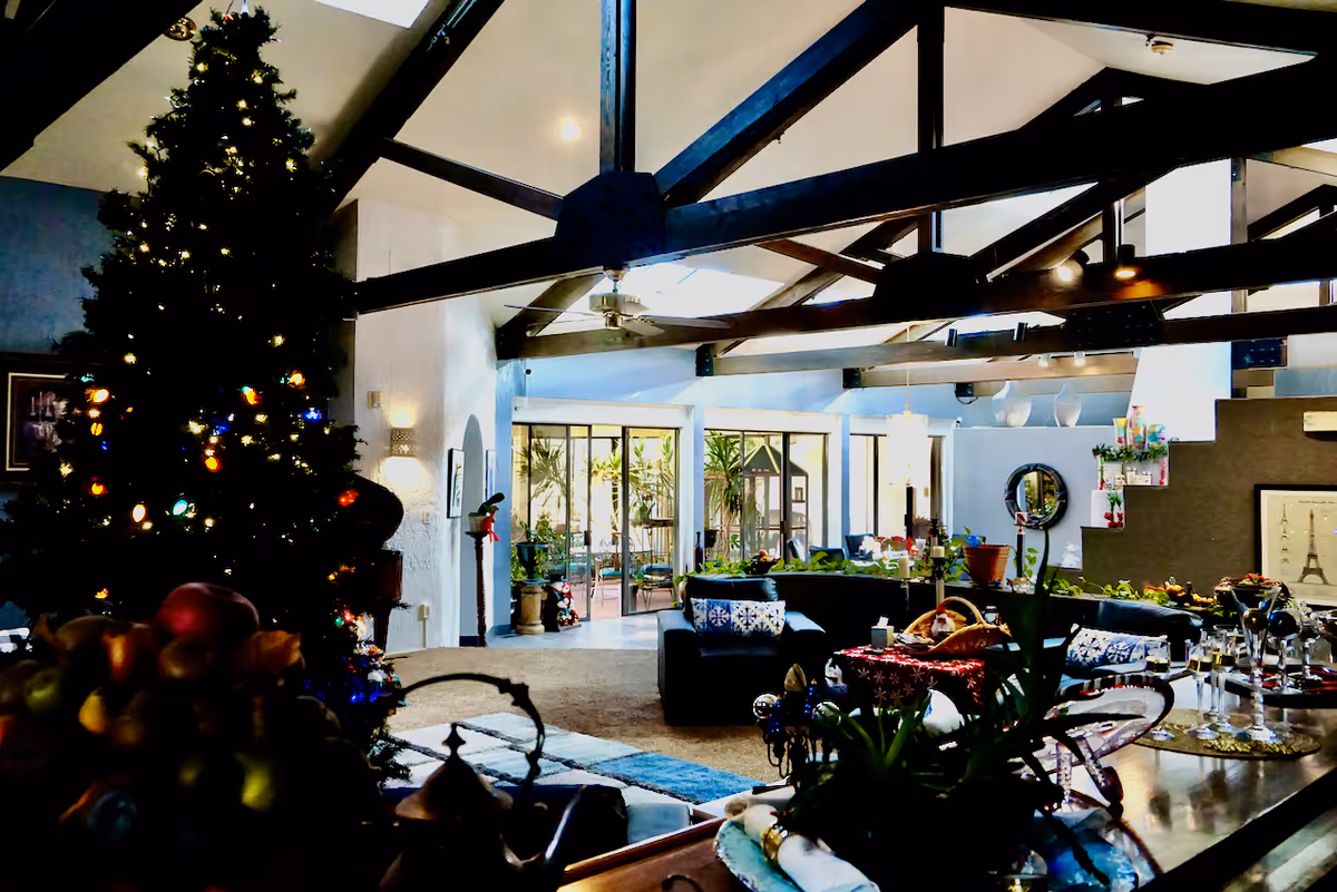 Spacious communal living room with exposed wooden beams, a decorated Christmas tree, sofas and a dining table.