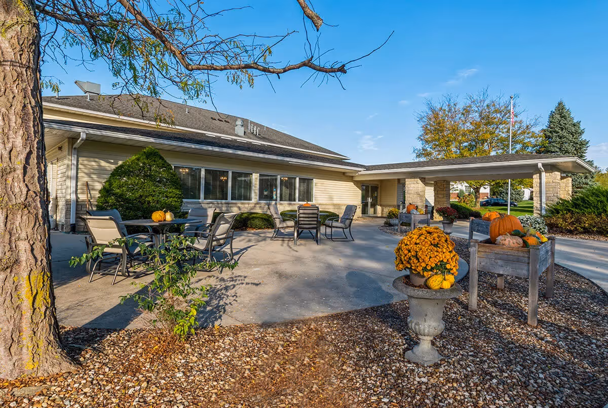 Outdoor seating patio and entrance of a senior living building decorated with pumpkins and potted mums.