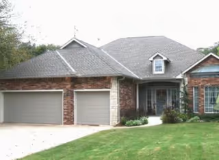 Front exterior view of a single-story brick house with a three-car garage, a small dormer window, and a well-maintained lawn.