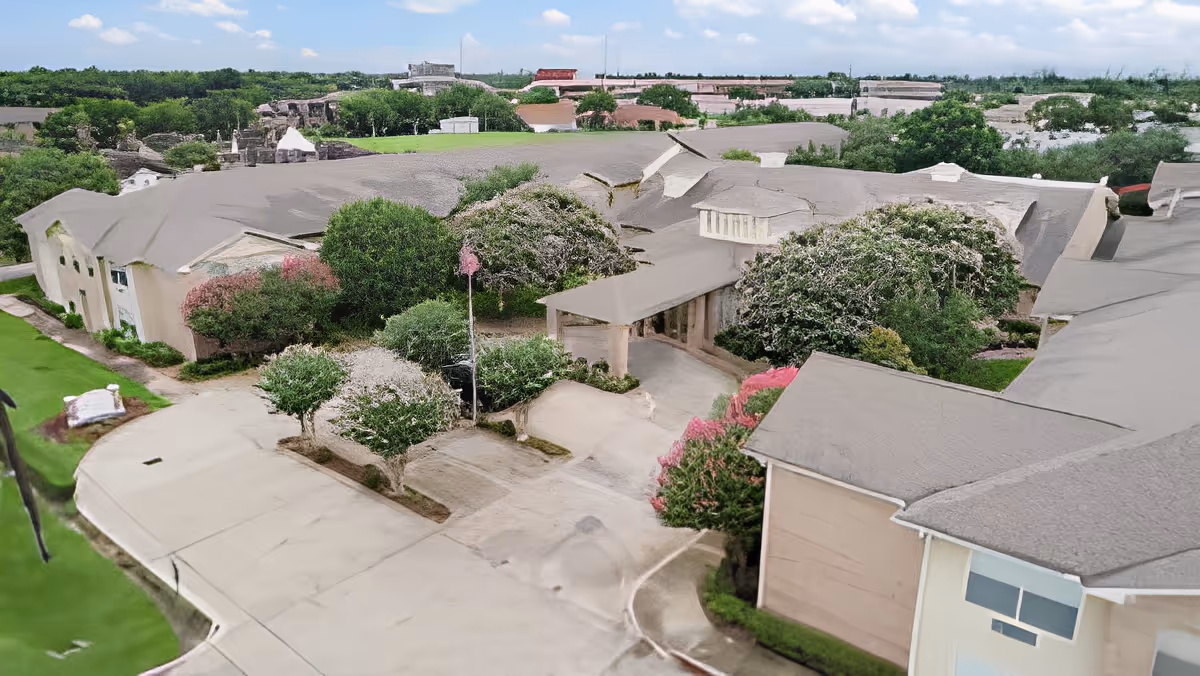 Aerial view of Morada Deer Park facility showing multiple connected buildings with gray roofs surrounded by green trees and landscaped bushes under a partly cloudy sky.
