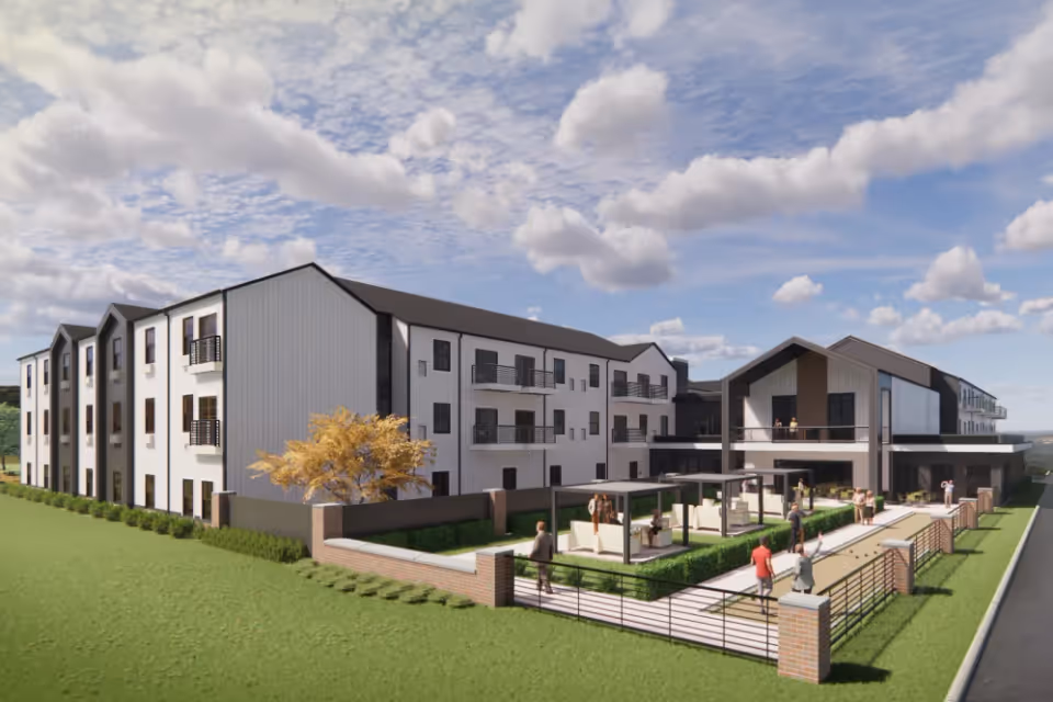 Exterior view of a modern three-story senior living facility named Mission Ridge with white and dark gray siding, balconies, and an outdoor patio area with seating and pergolas. Several people are walking and sitting in the outdoor space under a partly cloudy sky.