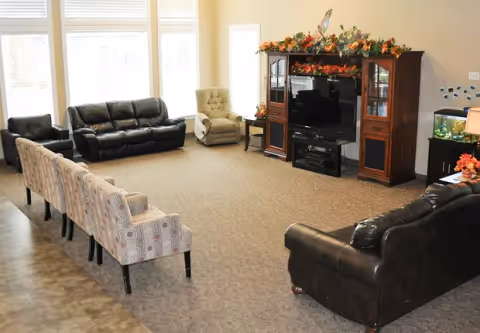 Spacious senior living lounge with multiple sofas and armchairs arranged around an entertainment center with a TV.