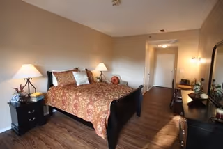 Furnished bedroom with a patterned bed, two nightstands with lamps, a dresser, and wood-look flooring.