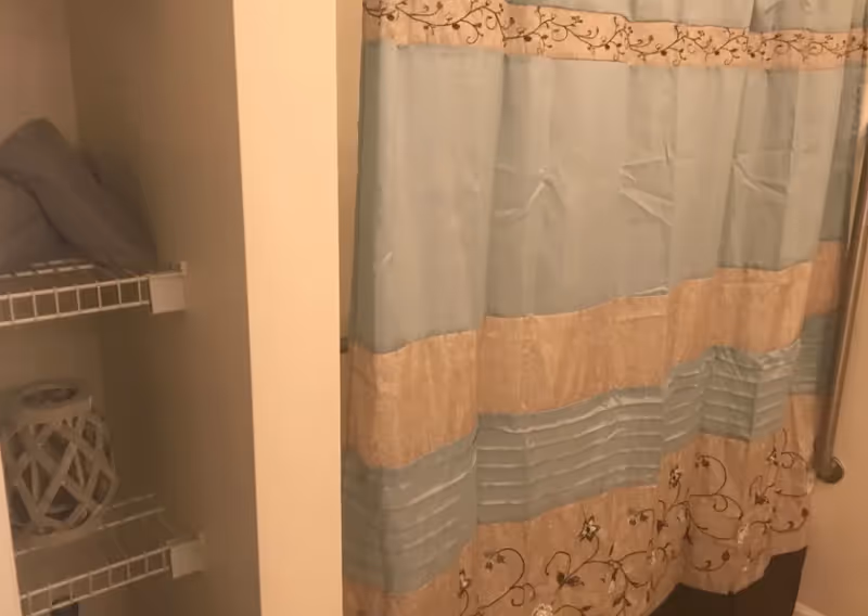 Decorative blue and beige shower curtain next to open shelving with folded towels and a decorative ceramic item.