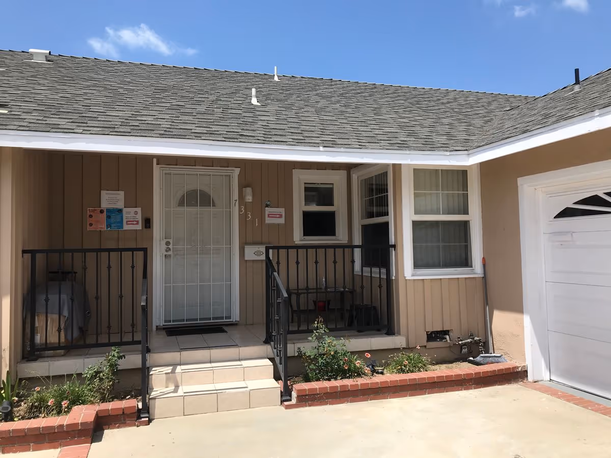 Front entrance of a single-story beige house with a small tiled porch, white security door, black metal railings, and an attached garage.