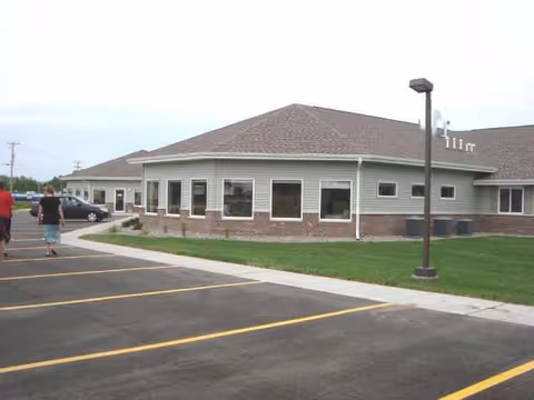 Exterior view of Mill St Manor building with parking lot and grassy lawn.