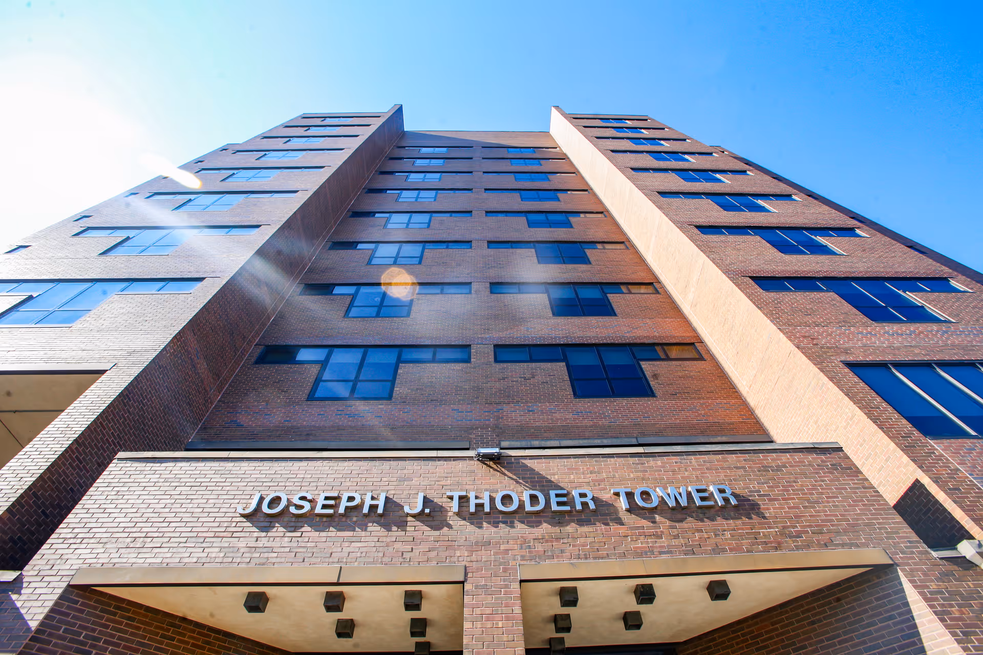 Low-angle view of the Joseph J. Thoder Tower, a multi-story brick building with rows of windows against a blue sky.