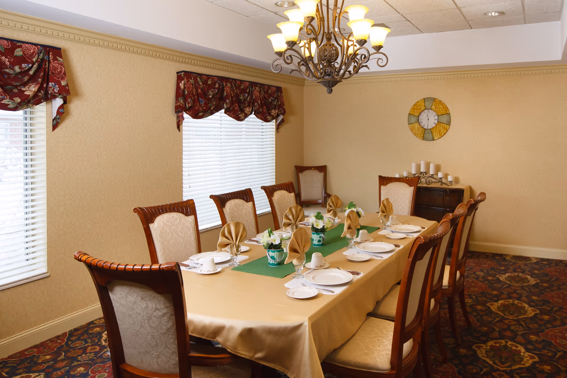 Formal dining room with a long table set with plates, folded napkins, floral centerpieces, and a chandelier.