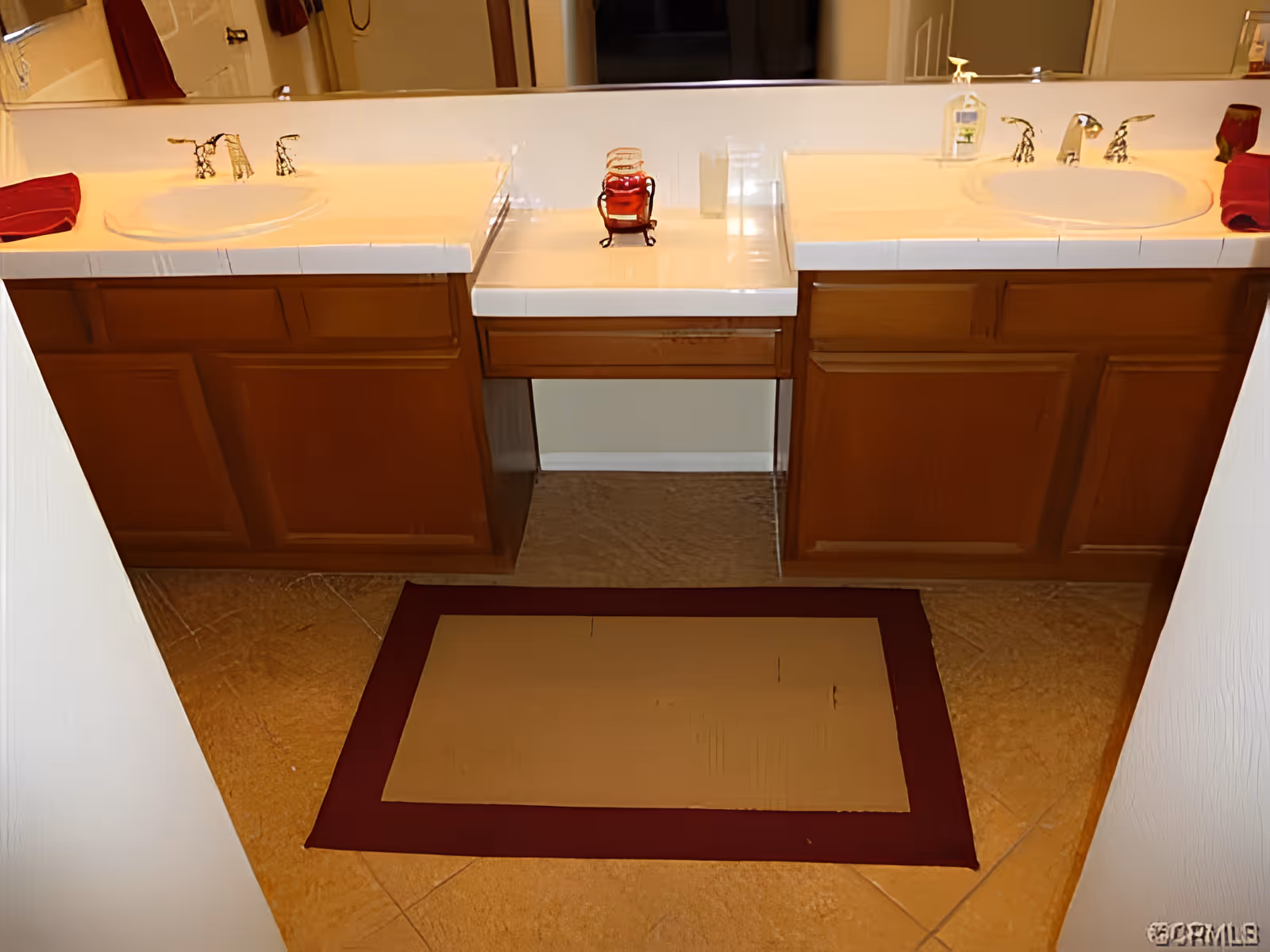 Double-sink bathroom vanity with wood cabinets, a large mirror, and a floor mat in front.