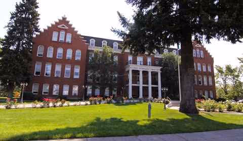 Brick academy-style building with white columns and manicured lawn in front.