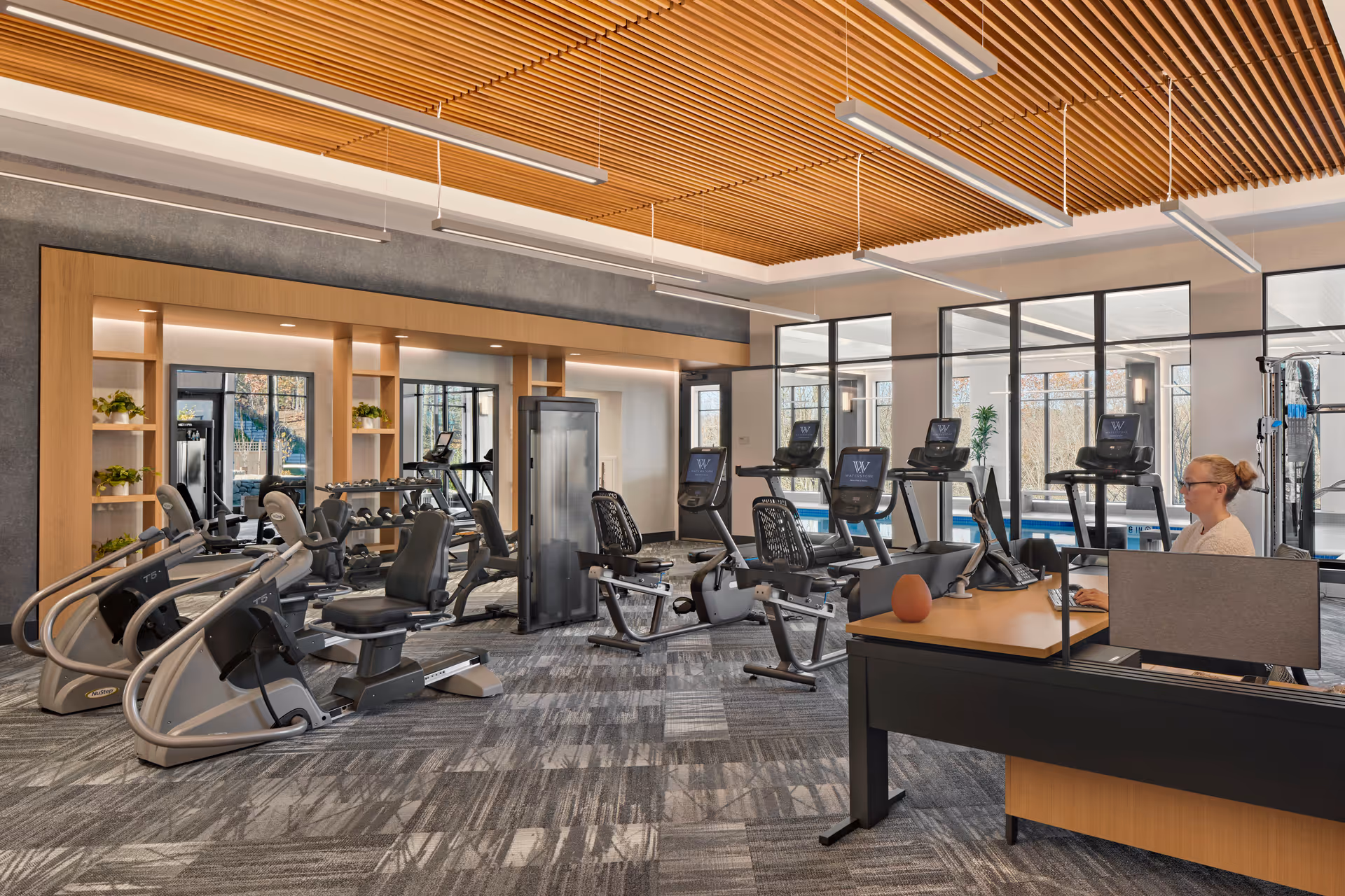 Bright, modern fitness center with cardio and strength equipment, a reception desk, and large windows.
