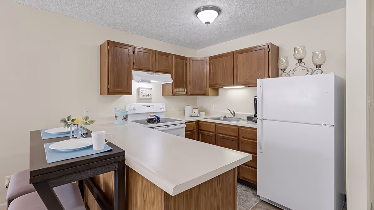 Small kitchen featuring wood cabinets, white refrigerator and stove, a sink and a breakfast bar set with two place settings.