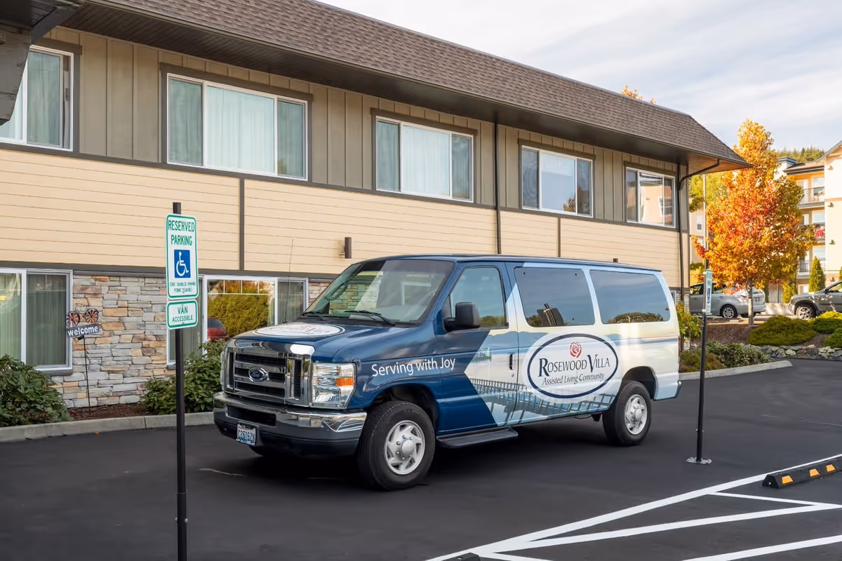 A Rosewood Villa shuttle van parked in a reserved accessible parking space in front of the facility building.
