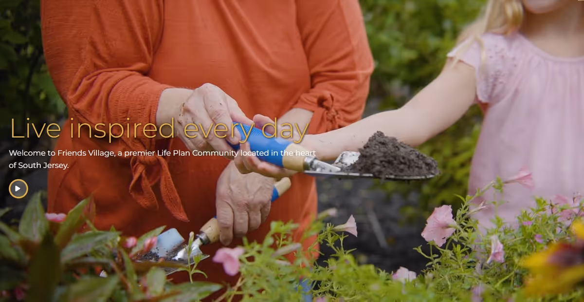 An older adult and a child gardening together, hands holding a trowel full of soil over flowering plants.