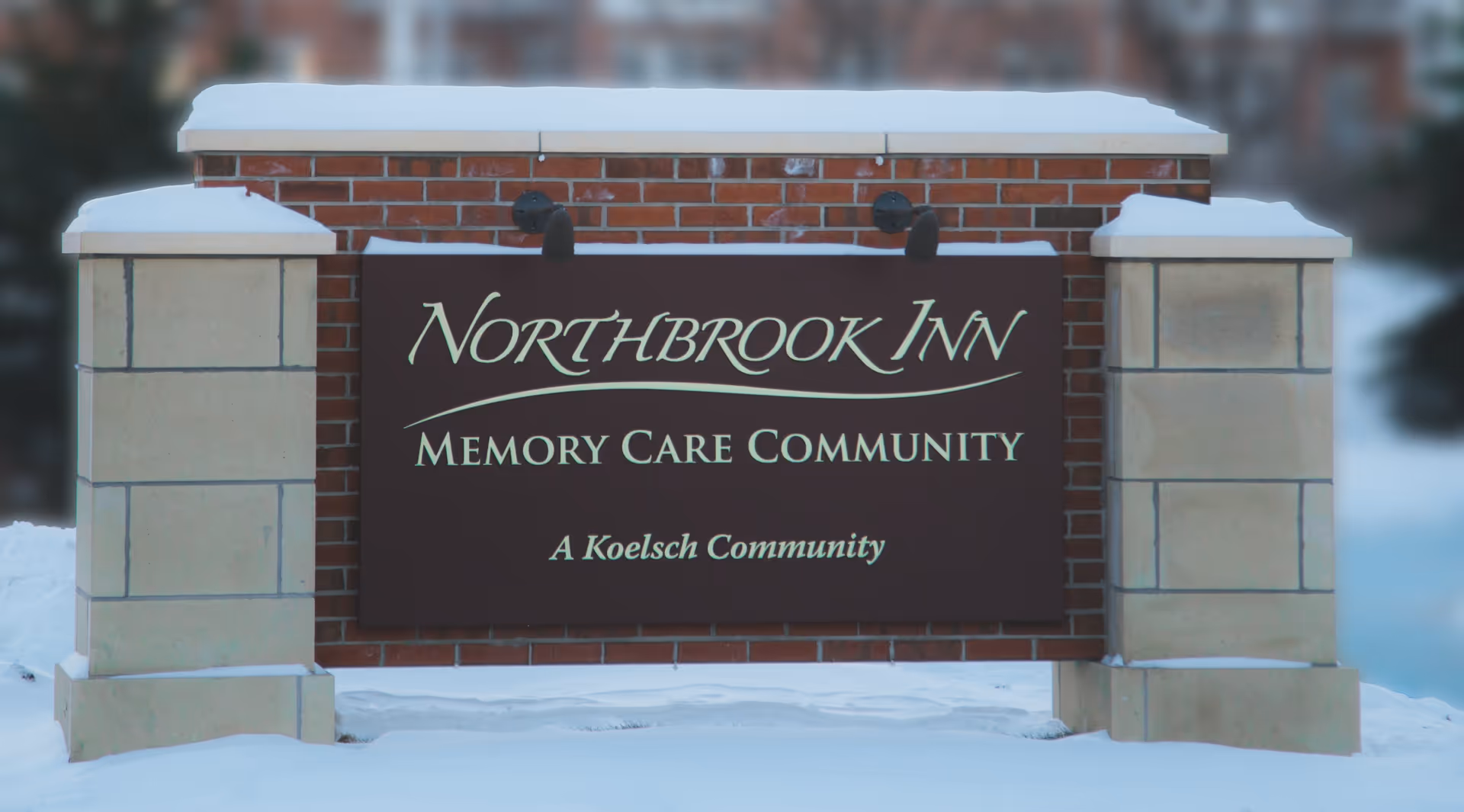 A brick and stone sign for Northbrook Inn Memory Care Community, with snow on the ground and on top of the sign.