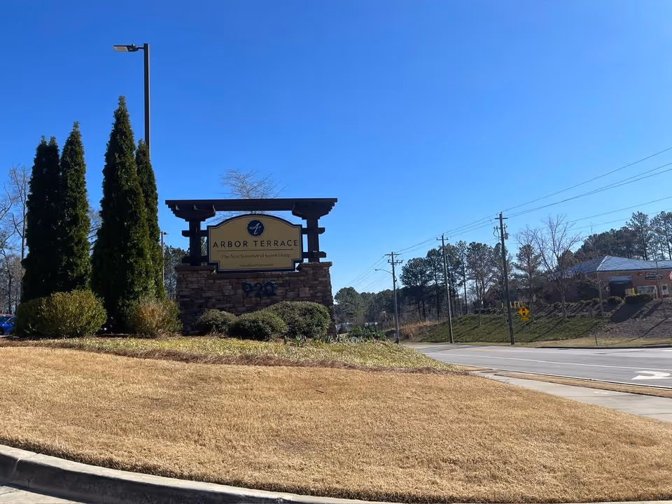 Stone entrance sign reading 'Arbor Terrace' on a landscaped lawn by the roadside under a clear blue sky.