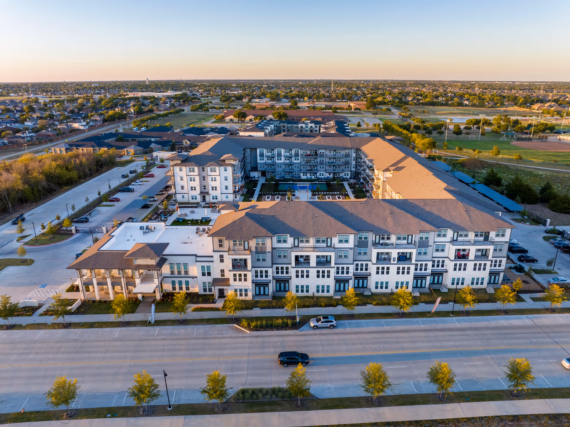 Aerial view of a large multi-story senior living facility named Amberlin at The Station, surrounded by parking lots, trees, and nearby residential neighborhoods under a clear sky.
