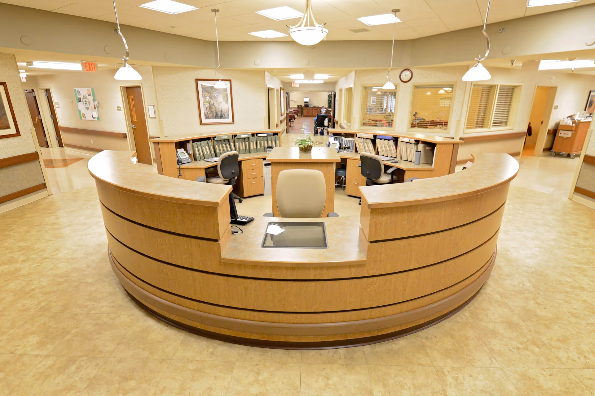 Curved wooden reception desk and nurse station in a bright, spacious interior hallway of a senior living facility.