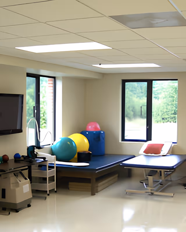 Therapy/rehab room with exercise balls, treatment tables, a TV, and windows.