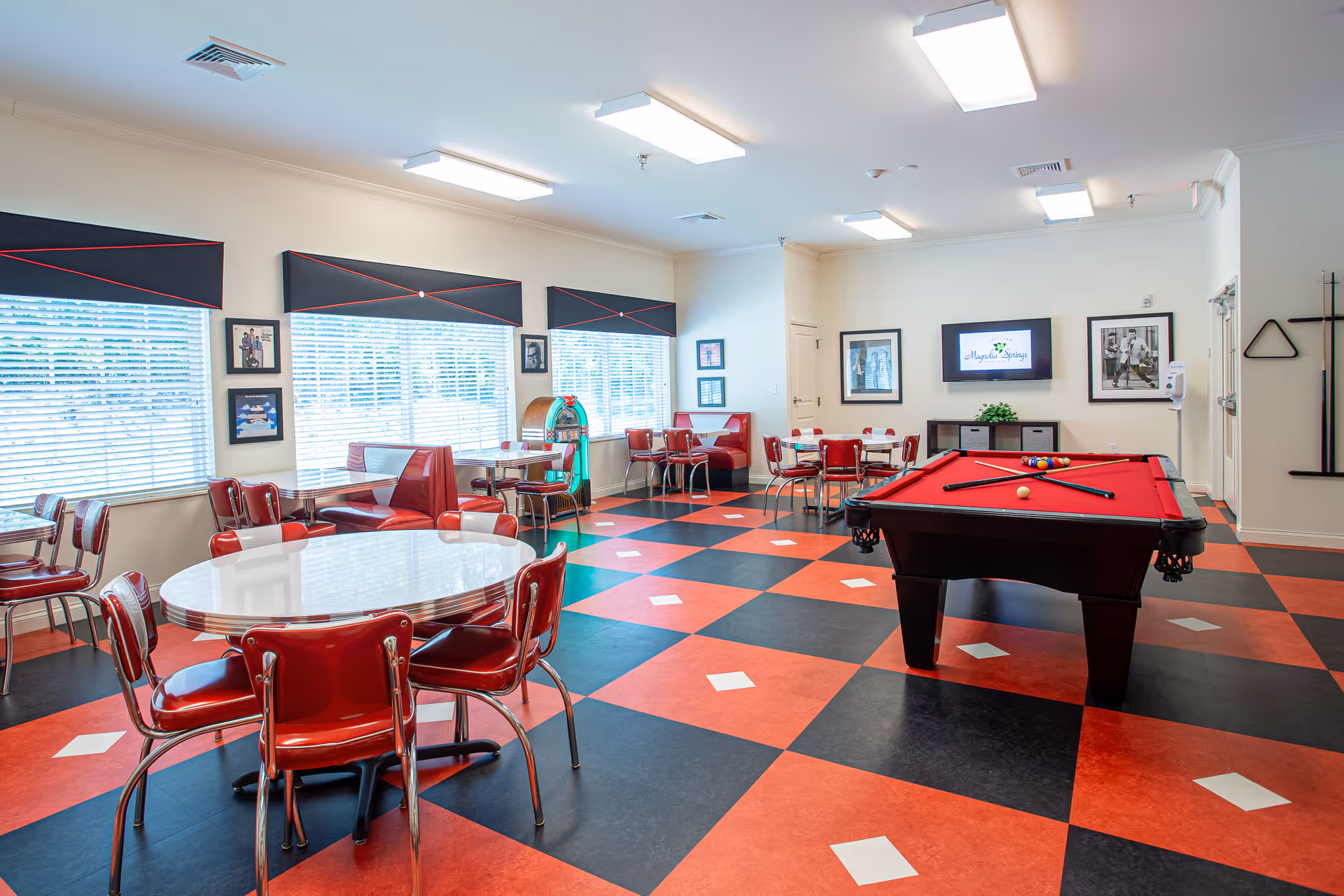 Bright games and dining room with red-and-black checkered flooring, diner-style seating, a red pool table and a jukebox.
