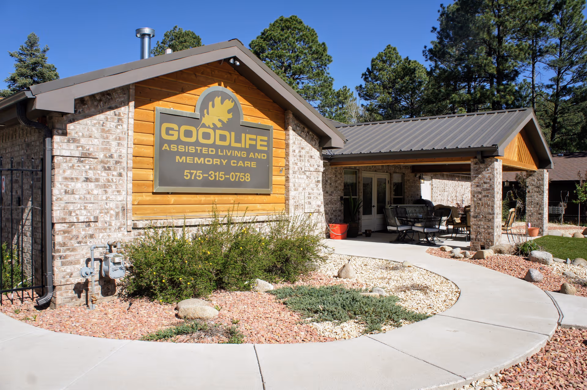 Front exterior of Goodlife Assisted Living and Memory Care building with sign, covered patio seating, and landscaped walkway.