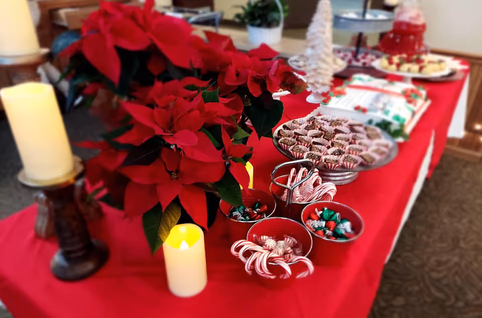 Holiday buffet table with a large red poinsettia, candles, bowls of candy canes and wrapped chocolates, and desserts on a red tablecloth.