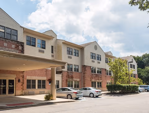 Two-story senior living facility with brick and beige siding, parking lot, and covered entrance.