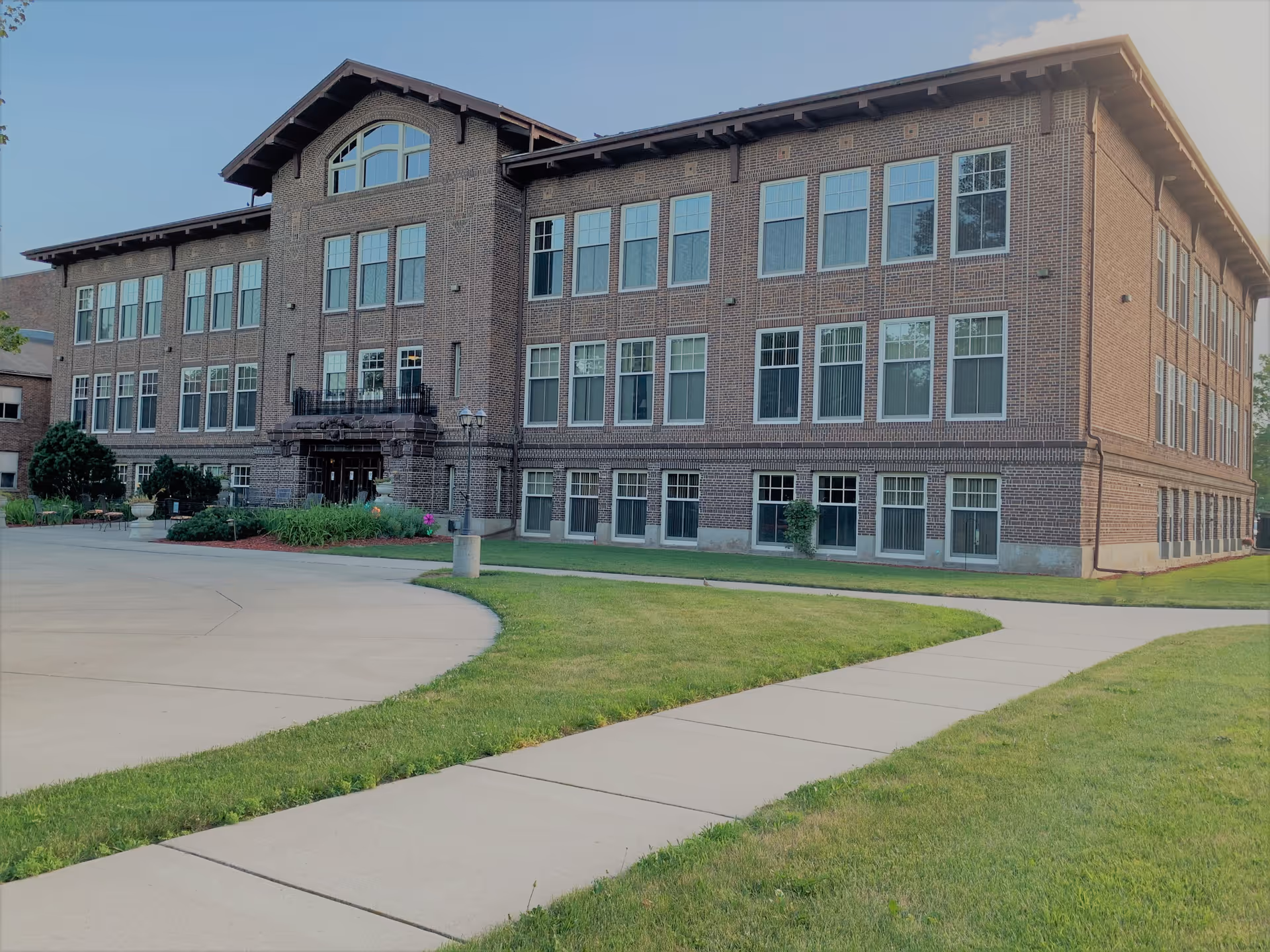 Exterior view of a large three-story brick building with many windows, surrounded by a well-maintained lawn and concrete walkways under a clear sky.