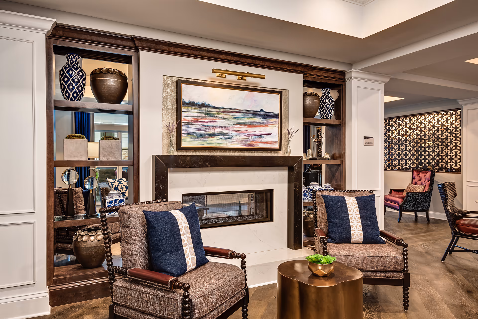 Elegant common lounge with two armchairs, a fireplace, built-in shelving, artwork, and a small table.