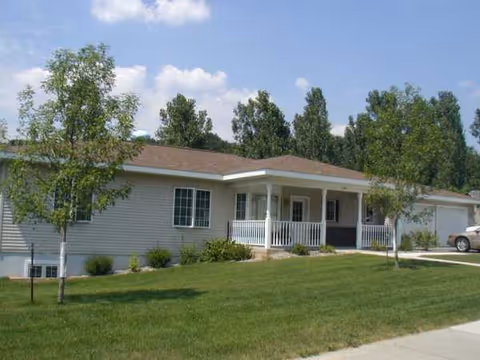 Front exterior of Clark Damon Villa senior living facility with porch, lawn, and trees.