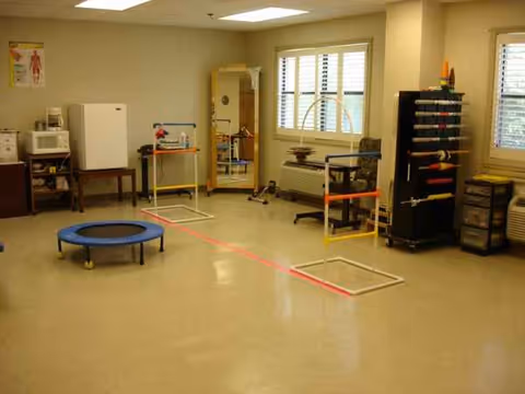 A spacious therapy room with exercise equipment and a window in a senior living facility.