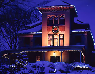 A snow-covered senior living facility's front entrance illuminated with festive holiday lights at night.