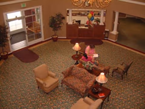 Overhead view of a furnished reception lobby with sofas, armchairs, table lamps, and a front desk where two people are seated.