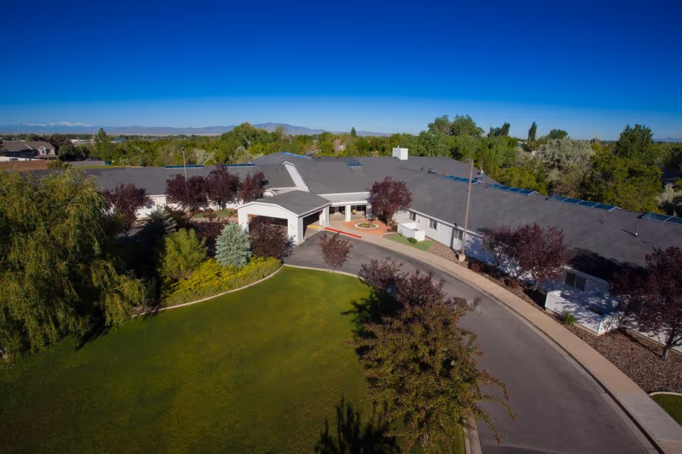 Aerial view of a single-story assisted living building with a covered front entrance, circular driveway and landscaped lawn and trees.