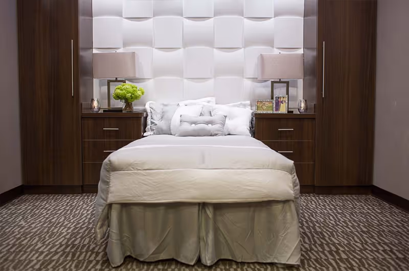 A neatly made bed centered between two wooden nightstands with lamps, decorative pillows, and a textured white headboard.