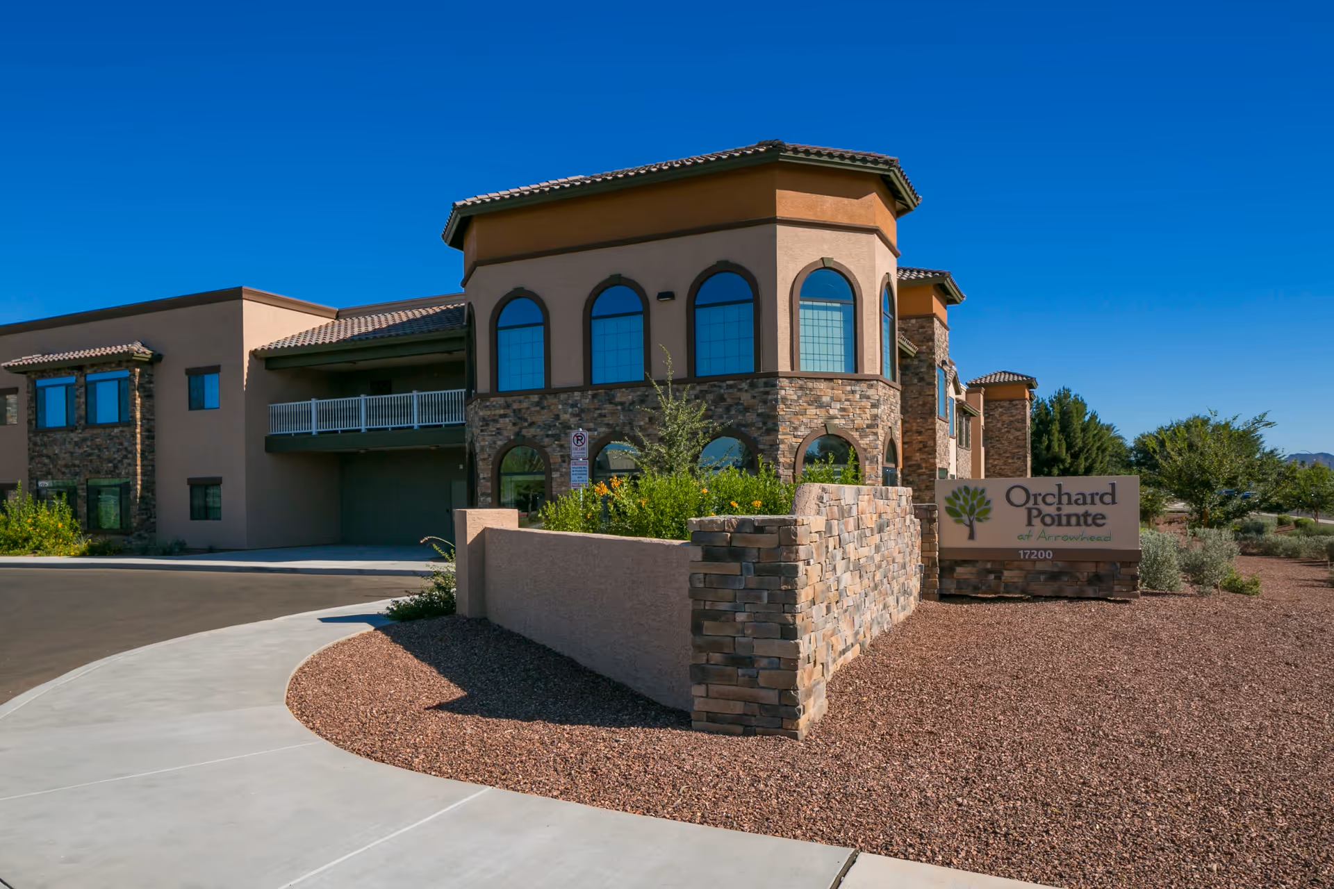 Front exterior of Orchard Pointe at Arrowhead building with stone accents, arched windows, and an entrance sign.