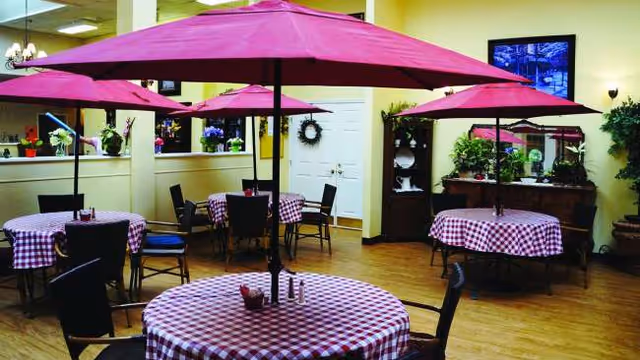 Indoor dining area with round tables, checkered cloths, and pink umbrellas.