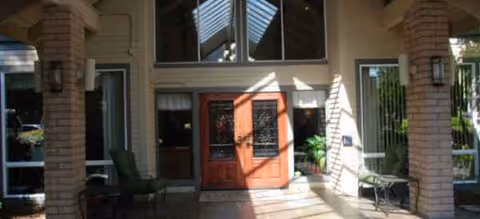 Entrance to Blossom Vale Senior Living featuring a wooden door and shaded porch seating.