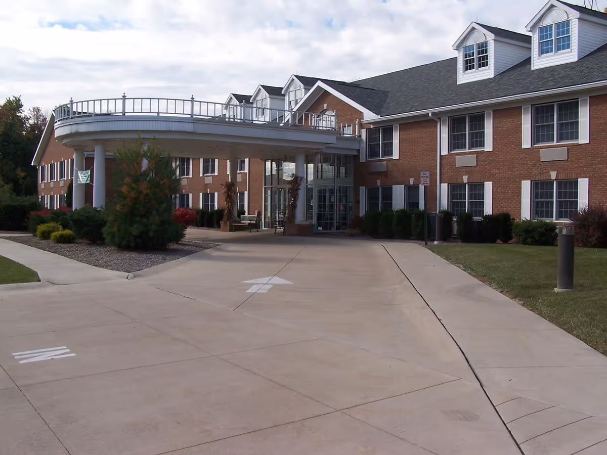Front entrance of a brick senior living building with a covered circular porte-cochere and driveway.