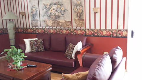 A cozy living room with maroon sofas, floral wallpaper, and a wooden coffee table.