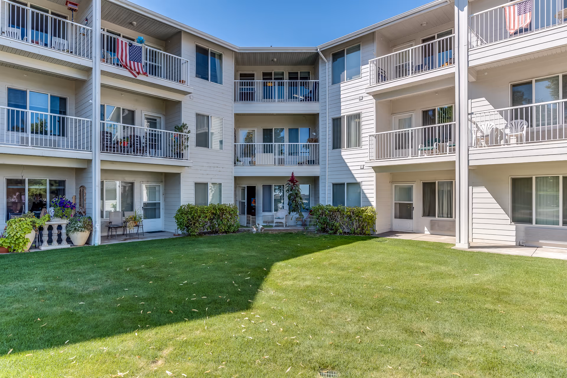 View of a three-story senior living building with balconies overlooking a green courtyard lawn.