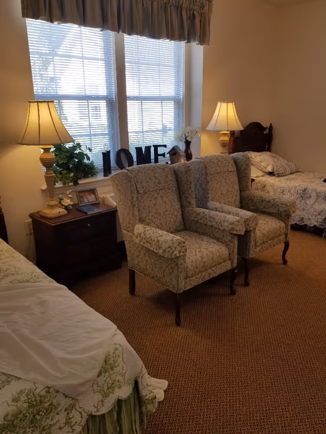 Cozy bedroom with two patterned armchairs in front of a window, bedside tables with lamps, and twin beds.
