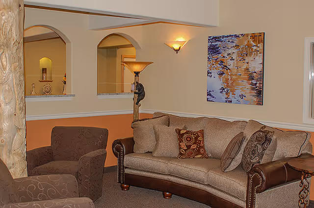 Living room seating area with a beige upholstered sofa, two patterned armchairs, a floor lamp, and wall artwork.
