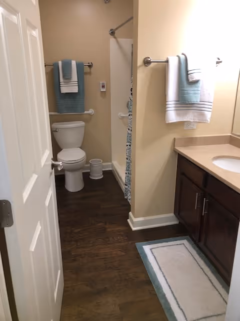 A bathroom with a toilet, shower stall, vanity with sink and cabinets, and towels hanging on racks.