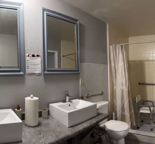 A shared bathroom with double sinks, mirrors, a toilet, and a curtained shower.